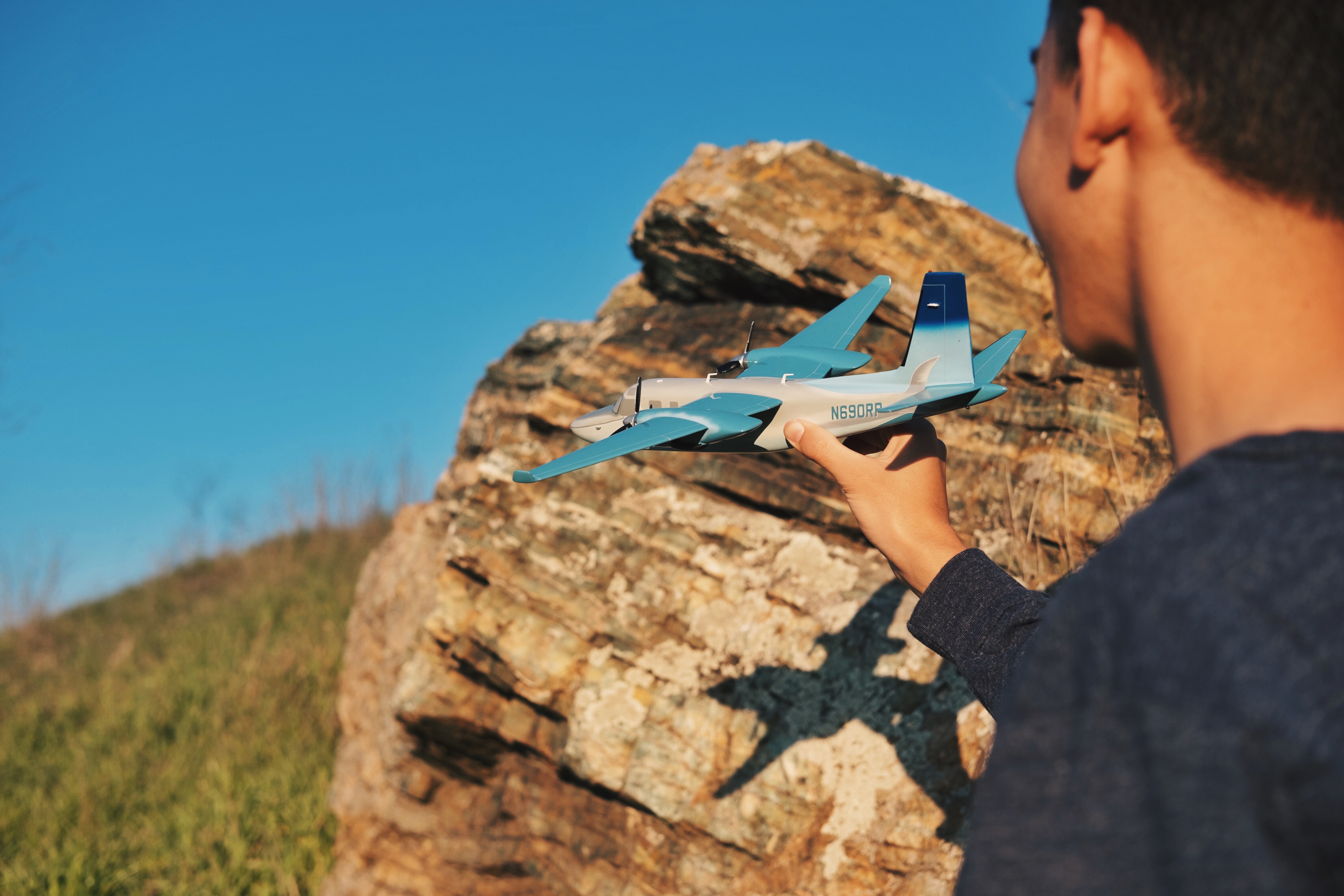 Picture of a man holding a model airplane about ready to launch it with a rock in the background 